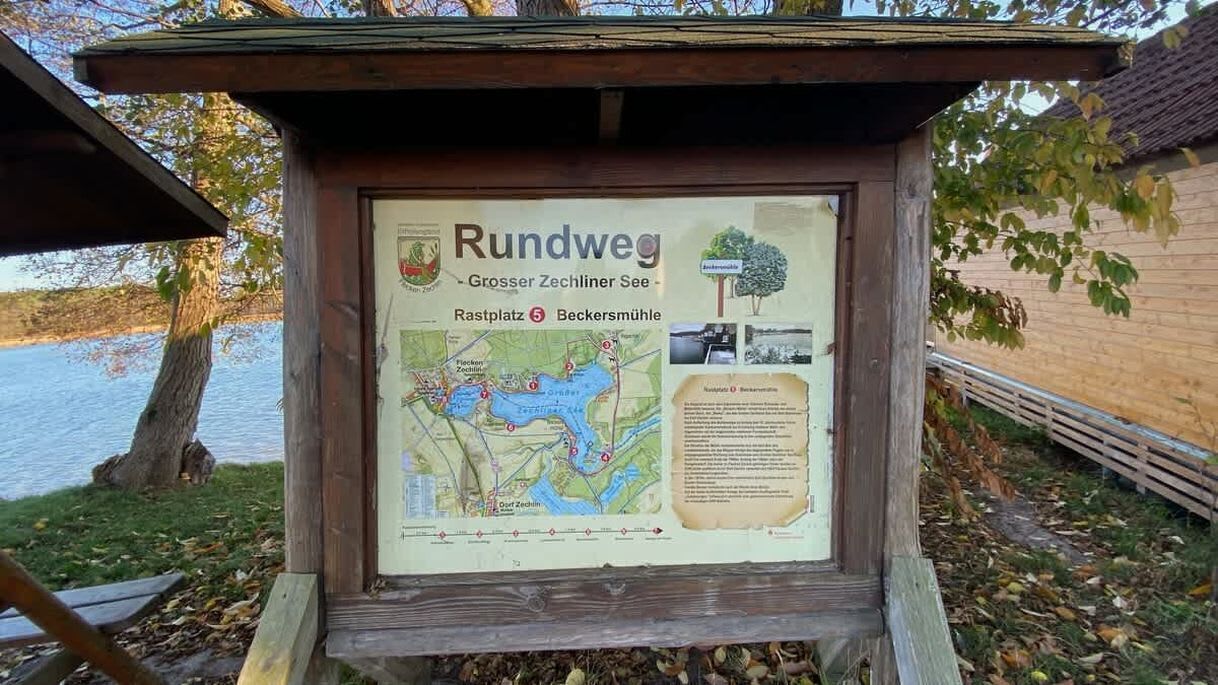 Um painel informativo de madeira com um mapa e texto sobre o Rundweg, o Grosserer Zechliner See e a Beckersmühle.