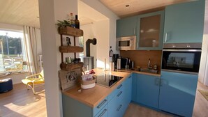Eine moderne Küche mit blauen Schränken, einer Mikrowelle, einem Backofen und einem eingebauten Herd. Im Vordergrund befindet sich eine Holztischplatte und ein Stuhl.