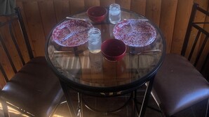 A round glass table with four red bowls and two small glass jars, set against a wooden wall with a view of a fenced outdoor area through large windows.