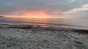 Une plage offrant une vue sur le coucher de soleil, avec un rivage sablonneux et une mer calme.