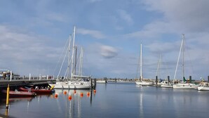 Un port de plaisance où sont amarrés de nombreux voiliers, une jetée anim ée par la présence de personnes, et une eau calme.