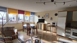 Un salon spacieux comprenant un canapé, une table à manger avec des chaises, un téléviseur et un coin cuisine avec des placards et un four à micro-ondes.