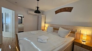 A neatly made bed with white linens and a folded towel, a bedside lamp, and a wooden headboard.