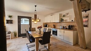 A modern kitchen with white cabinets, a wooden dining table, and a hanging light fixture.