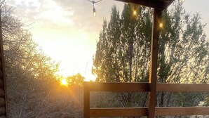 Un bain à remous doté d’une terrasse en bois et illuminé de guirlandes lumineuses, entouré d’arbres et avec un coucher de soleil en toile de fond.