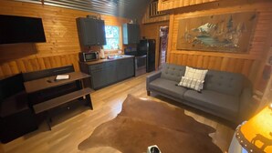 Un intérieur de chalet chaleureux avec une table à manger, un canapé, un coin cuisine et un téléviseur fixé au mur.