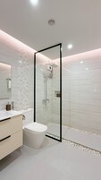 Un baño moderno con ducha acristalada, inodoro y tocador con espejo.