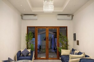Una sala de estar moderna con un ventanal que da a una cocina, dos equipos de aire acondicionado y una araña.