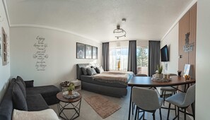 Een moderne, compacte leefruimte met een bank, een klein rond tafeltje, een bed en een eethoek.