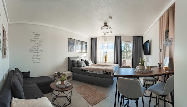A modern, compact living space with a sofa, a small round table, a bed, and a dining area.