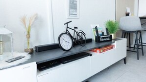 A modern living room with a mounted TV, a bicycle, a clock, and a remote control on a white entertainment unit. - Little Oasis Brilon-Willingen (Brilon)