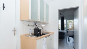 A compact kitchen with a stove, coffee maker, and cabinets. A dining area with a table and chairs is visible through an open doorway. - Little Oasis Brilon-Willingen (Brilon)