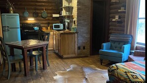 A rustic cabin interior with a wooden dining table, a blue armchair, a sofa with a patterned cover, a kitchen area with a Galanz refrigerator, and a cowhide rug. - Secluded Escape with a hot tub, surrounded in nature (BLUFFDALE)