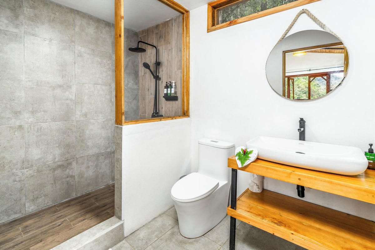 A bathroom with a wooden shower, white toilet, and a sink with a mirror above it.