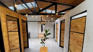 A hallway with wooden walls and a bench, leading to a room with a large window and a plant. - RIOS LODGE (Pacuarito)