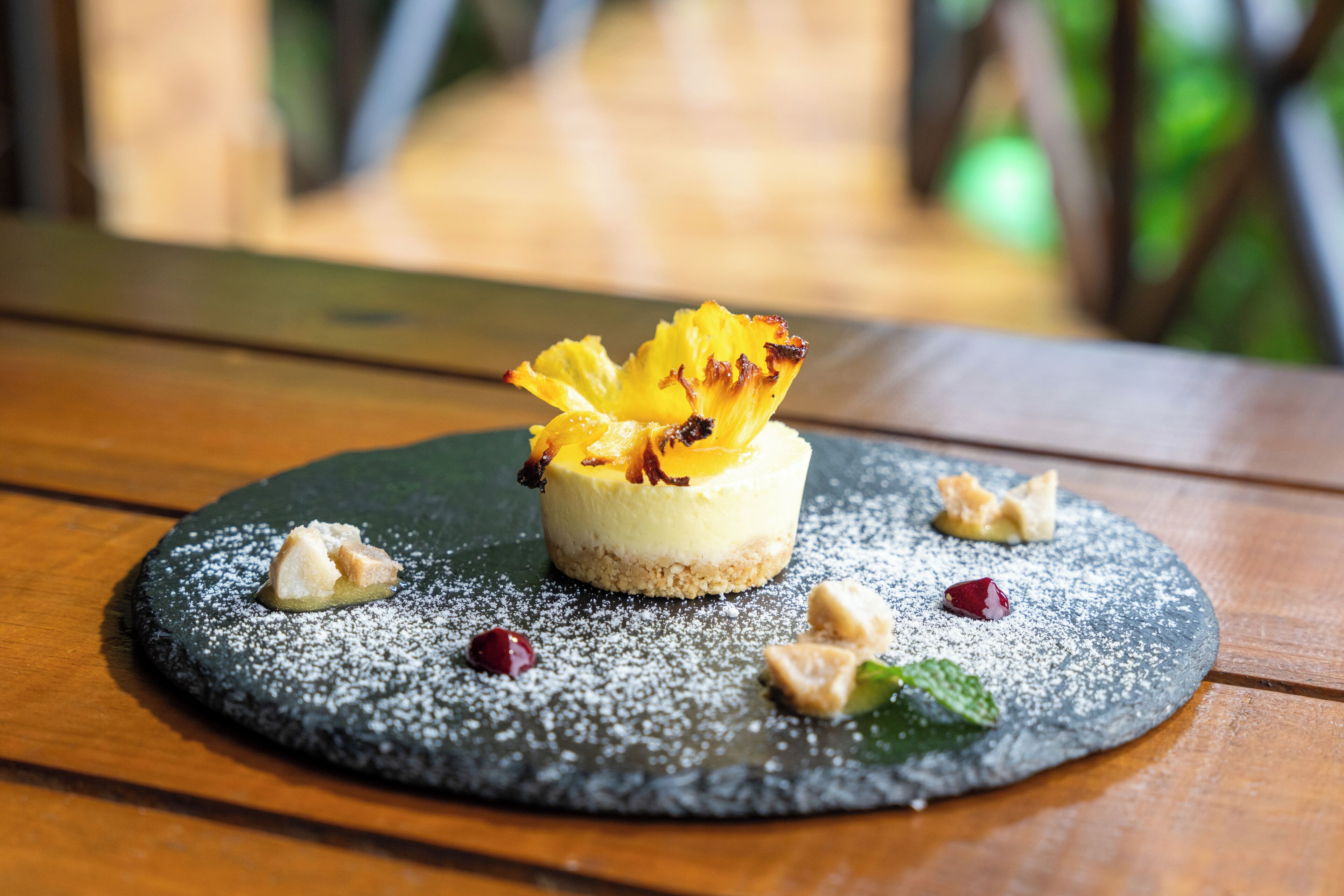 A dessert on a slate plate with powdered sugar, nuts, and a fruit garnish.