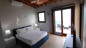 A bedroom with a bed, nightstands, a ceiling fan, a TV, and a sliding glass door to a balcony. - Charming 2bdrm/2bath beachfront PH Condo WiFi, AC, TV, beach lounges included (Philipsburg)