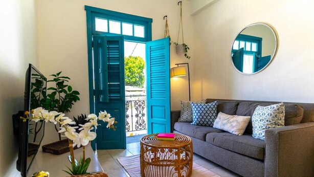 Una sala de estar con un sofá gris, una mesa de centro de mimbre y una puerta azul.