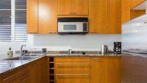 Una cocina con armarios de madera, un lavamanos de acero inoxidable, un microondas y una cafetera.