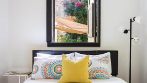 Una cama con colchón blanco, cabecera negra y almohadas estampadas de colores.