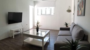 A modern living room with a flat-screen TV, a glass coffee table, a grey sofa, and two potted plants. - Private Pool Piscina Privada by CasaSaffra (San Juan)