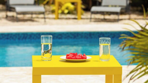 A yellow table with two glasses of water and a plate of watermelon by a pool. - Private Pool Piscina Privada by CasaSaffra (San Juan)