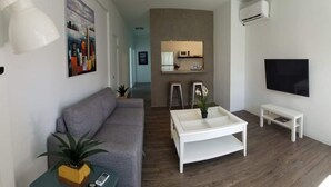 A modern living room with a grey sofa, a white coffee table, a TV, and a small white table. - Private Pool Piscina Privada by CasaSaffra (San Juan)