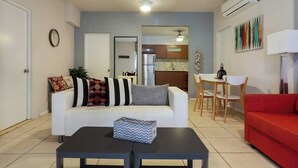 A living room with a white sofa, a red couch, a dining table with chairs, and a kitchen in the background. - 5 Bedroom with Private Pool NEXT TO BEACH (San Juan)