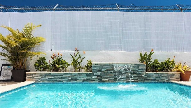 A swimming pool with a waterfall feature, surrounded by potted plants and a white fence. - 5 Bedroom with Private Pool NEXT TO BEACH (San Juan)
