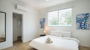 Een slaapkamer met een groot bed, een raam met zonwering, een wandairconditioner en een handdoekrek.