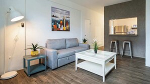 Een moderne woonkamer met een grijze bank, een witte salontafel, twee potplanten, een vloerlamp en een schilderij aan de muur.