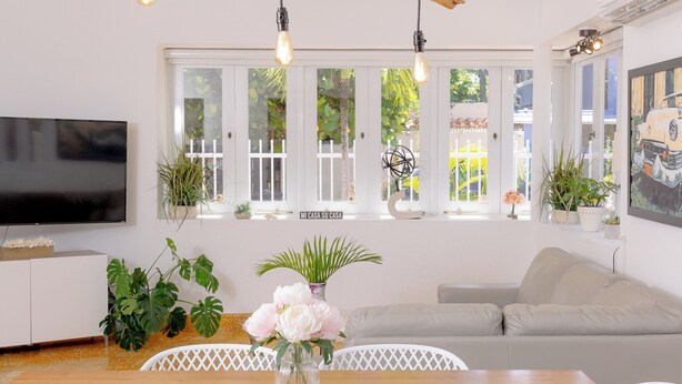 A modern living room with a wooden branch chandelier, a flat-screen TV, a dining table with a vase of flowers, and a sofa. - Extra Large Spacious Beach House with Solar Panels and 800 gallon cistern (San Juan)
