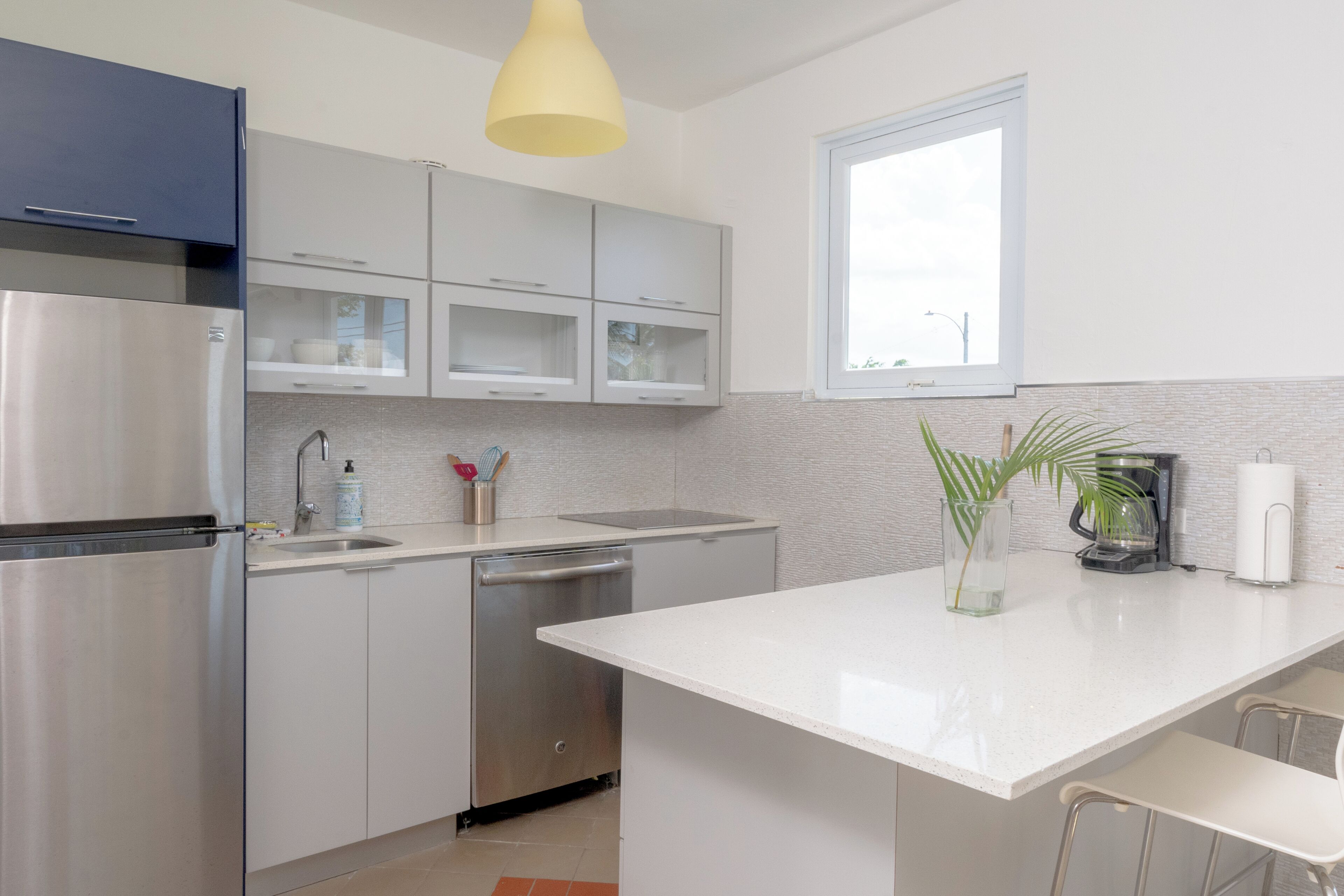 A modern kitchen with stainless steel appliances, white cabinetry, a central island, and a window providing natural light.