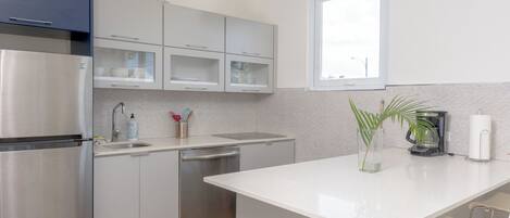 A modern kitchen with stainless steel appliances, white cabinetry, a central island, and a window providing natural light.