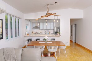 Cozinha moderna com armários brancos, mesa de jantar de madeira e um lustre único em forma de galho de árvore.