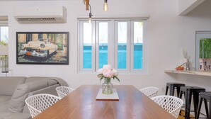 A dining area with a wooden table, white chairs, a vase with flowers, and a painting of a car on the wall. - Extra Large Spacious Beach House with Solar Panels and 800 gallon cistern (San Juan)