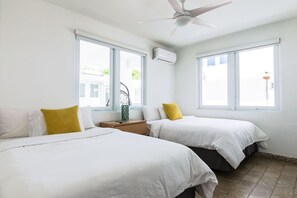 Een hotelkamer met twee bedden, een plafondventilator en grote ramen.