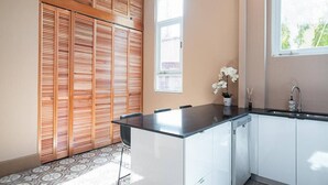 Een kleine keuken met een zwart aanrecht, witte kastjes, een houten lambrisering, een raam en een potorchidee.