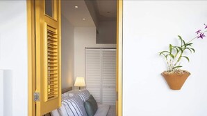 Una habitación con cama, lámpara de noche, ventana con persianas y una planta en maceta.