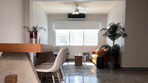 A spacious living area with a dining table, a sofa, and a coffee table. There are potted plants and a ceiling fan.