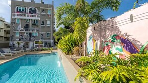 A swimming pool with lounge chairs, a multi-story building with balconies, and a mural on the wall.