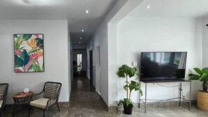 Un moderno vestíbulo de hotel con un largo pasillo, un televisor de pantalla plana, sillas de mimbre y un cuadro abstracto y colorido.