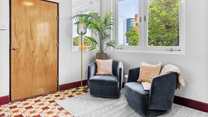A room with a wooden door, two dark armchairs, a patterned rug, a floor lamp, and a window with a view of trees and buildings. - Location is Everything  3and a Half  Bedroom (San Juan)
