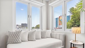 A modern bedroom with a large bed, multiple pillows, a bedside table with a lamp, and large windows offering city views. - Location is Everything  3and a Half  Bedroom (San Juan)
