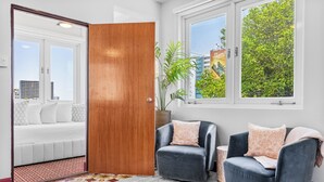 A modern living room with a large wooden door, two dark armchairs with patterned cushions, a small side table, and a view of a cityscape through a window. - Location is Everything  3and a Half  Bedroom (San Juan)