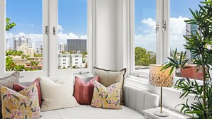 A modern bedroom with a city view, a sofa with multiple cushions, and a bedside table with a lamp. - Tropical San Juan Life with Pool (San Juan)