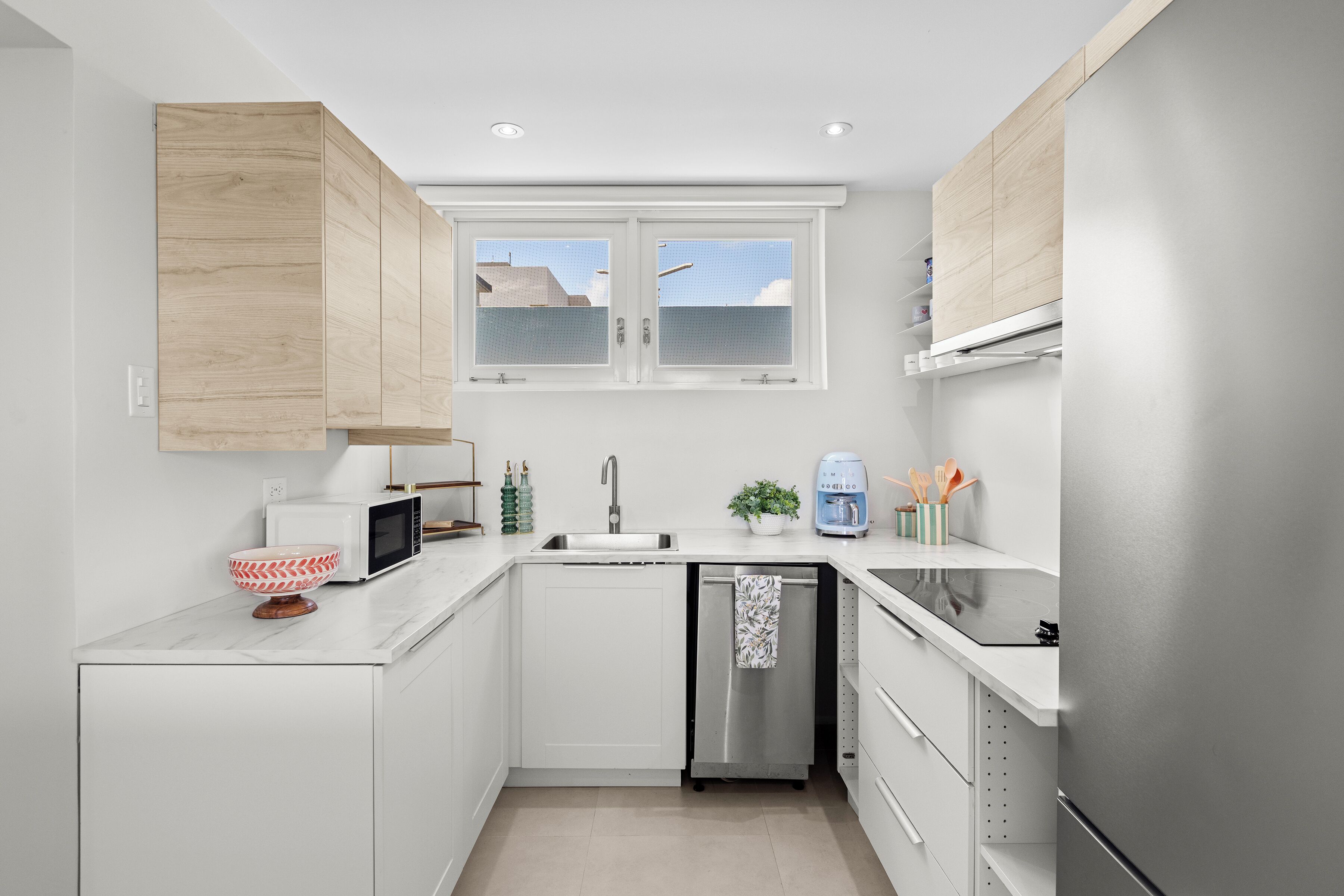Una cocina moderna con armarios blancos, lavavajillas integrado, microondas y cafetera.