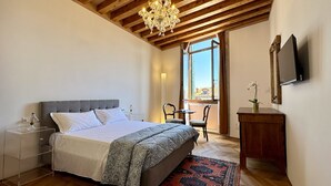 Une chambre à coucher comprenant un lit, une table de chevet, une lampe, une chaise, un bureau, une télévision et une fenêtre donnant sur un beau paysage.