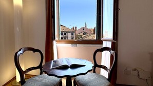 Une pièce avec une table et deux chaises, une fenêtre donnant sur des immeubles et une prise électrique au mur.