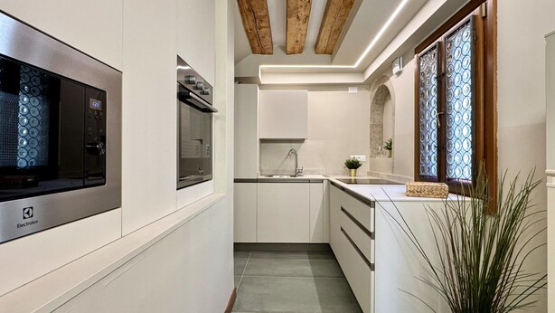 Une cuisine moderne avec des meubles blancs, un four encastré et une grande fenêtre ornée de vitraux.